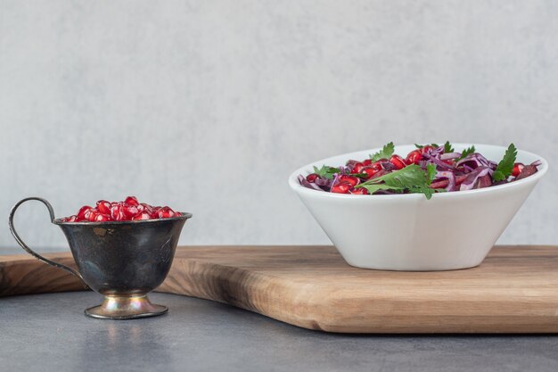 Tazón de fuente de ensalada de verduras sobre tabla de madera con semillas de granada. Foto de alta calidad