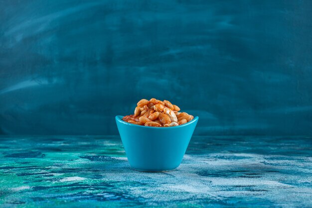Tazón de fuente de frijoles al horno, sobre la mesa azul.