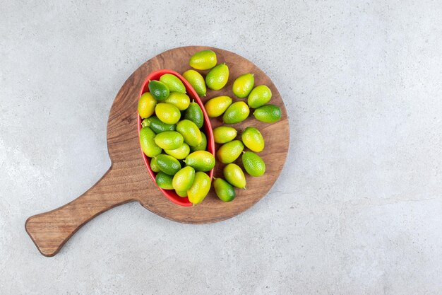 Tazón de fuente de kumquats junto a un montón sobre una tabla de madera en el fondo de mármol. Foto de alta calidad