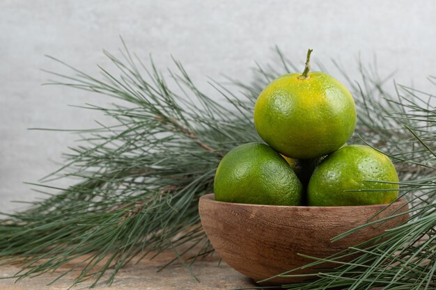 Tazón de fuente de mandarinas frescas en mesa de mármol con rama.