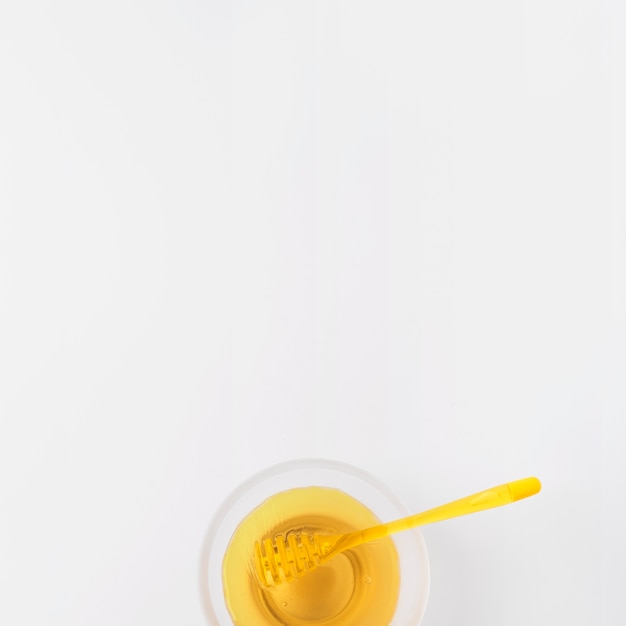 Tazón de fuente de miel con cucharón en superficie blanca