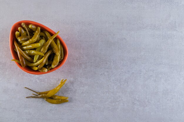 Tazón de fuente naranja de chiles en escabeche en la mesa de piedra.