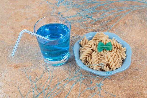 Tazón de fuente de pasta fusilli y copa de cóctel azul sobre fondo de mármol. Foto de alta calidad