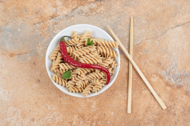 Tazón de fuente de pasta fusilli con pimienta y palillos en la mesa de mármol. Foto de alta calidad