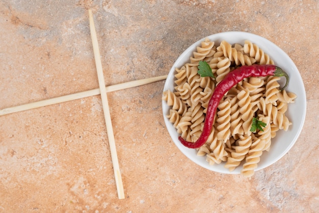 Tazón de fuente de pasta fusilli con pimienta y palillos de mesa de mármol