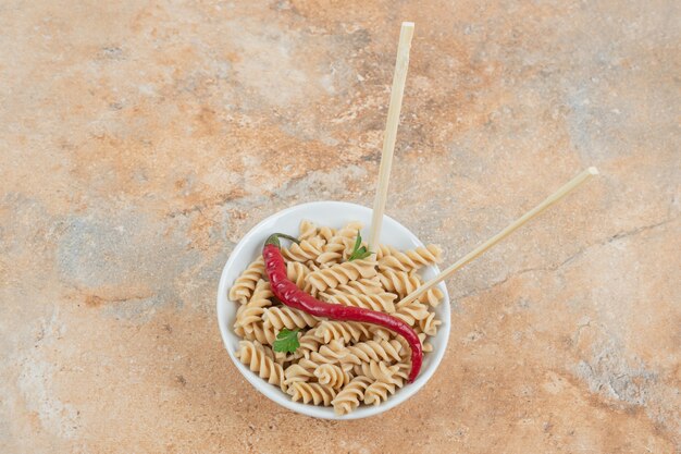 Tazón de fuente de pasta fusilli con pimienta y palillos de mesa de mármol