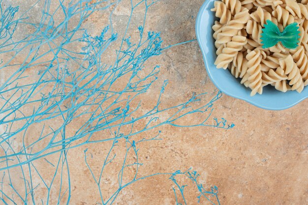 Tazón de fuente de pasta fusilli con planta azul sobre fondo naranja