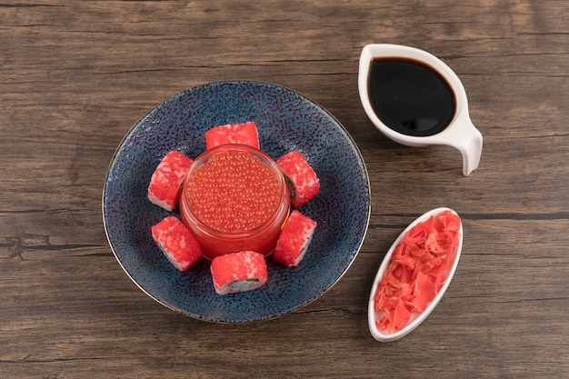 Tazón de fuente de rollos de sushi y caviar rojo sobre mesa de madera con soja y jengibre