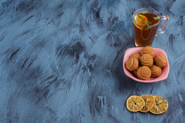 Tazón de fuente rosa de mini tortas de canela con un vaso de té sobre fondo de piedra.