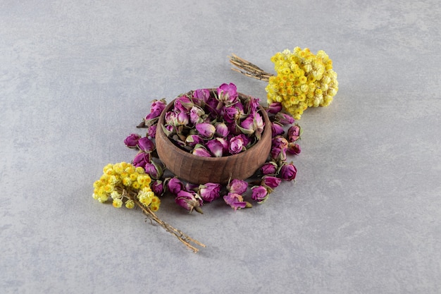 Tazón de fuente de rosas en ciernes y flores amarillas sobre fondo de piedra.