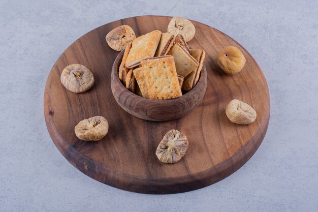 Tazón de fuente de sabrosas galletas crujientes e higos secos sobre tabla de madera.