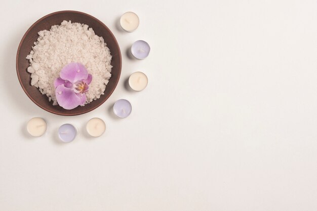 Tazón de fuente de la sal de baño con la flor de la orquídea adornada con las velas en el fondo blanco