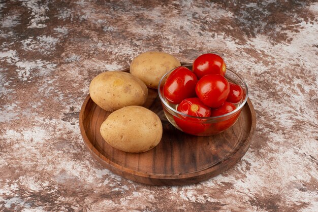 Tazón de fuente de tomates encurtidos y patatas hervidas en placa de madera.