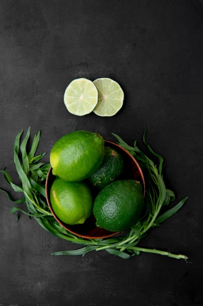 Foto gratuita tazón de limas con rodajas de limón y estragón sobre superficie negra