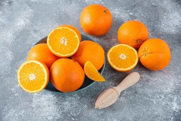 Un tazón lleno de frutas de naranja jugosas en rodajas y enteras con escariador de madera.