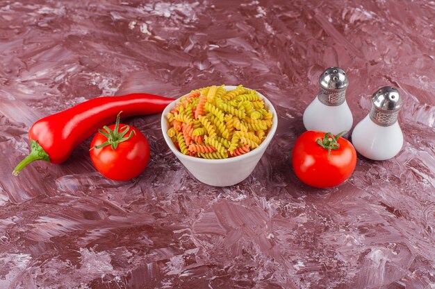 Un tazón de pasta espiral cruda multicolor con tomates rojos frescos y ají.