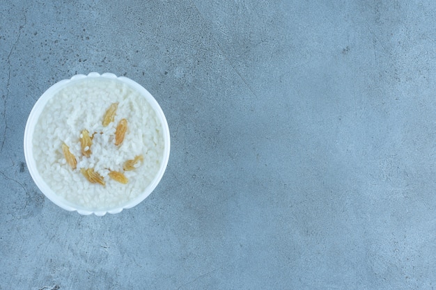 Tazón pequeño de avena cubierto con un puñado de pasas sobre mármol.