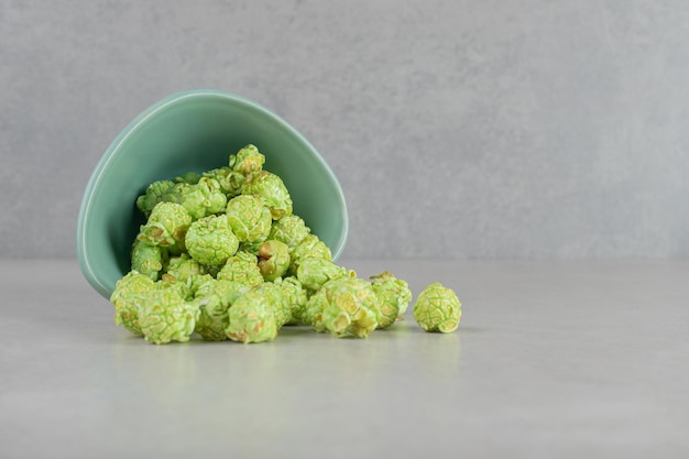 Foto gratuita tazón pequeño caído, derramando palomitas de maíz confitadas verdes sobre fondo de mármol.