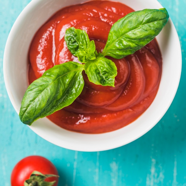 Tazón de salsa de tomate y albahaca sobre fondo turquesa