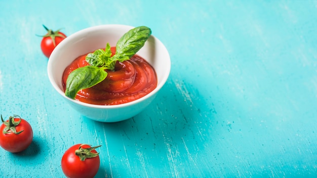 Tazón de salsa de tomate y albahaca y tomates frescos sobre fondo turquesa