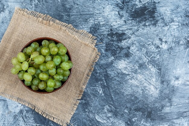 Un tazón de uvas blancas sobre un mantel sobre fondo de mármol azul oscuro, plano laical.