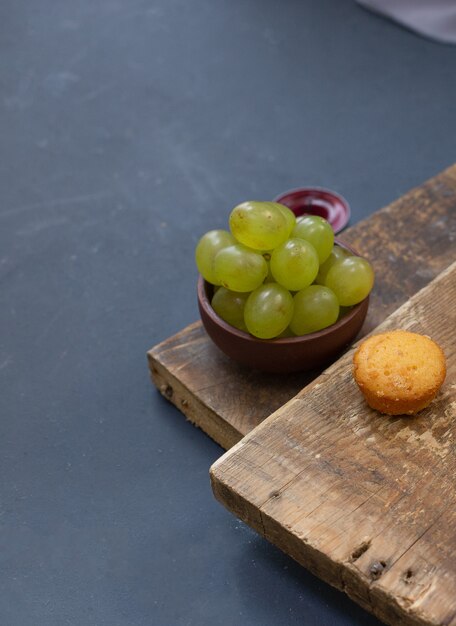 tazón de uvas verdes y un muffin de vainilla en el pedazo de madera