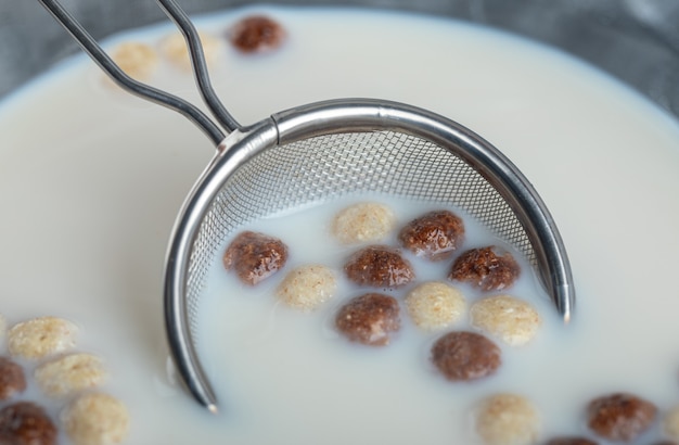 Foto gratuita un tazón de vidrio con bolas de cereales deliciosos para el desayuno y colador.