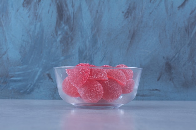 Un tazón de vidrio lleno de caramelos de gelatina azucarados rojos sobre la mesa gris.