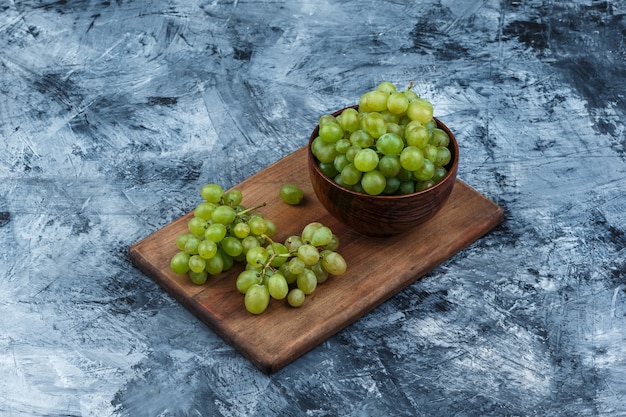 Foto gratuita tazón de vista de ángulo alto de uvas blancas en la tabla de cortar sobre fondo de mármol azul oscuro. horizontal