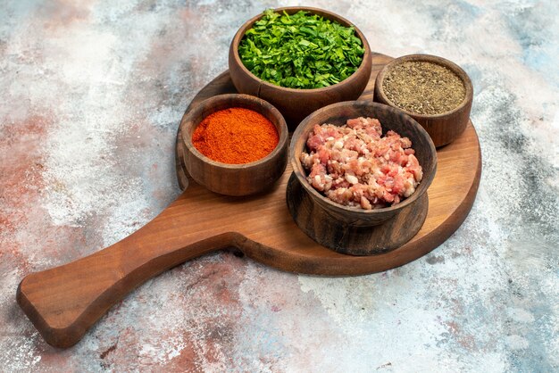 Tazón de vista frontal con tazones de carne con verduras diferentes especias en una tabla de cortar sobre fondo gris comida