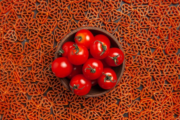 Tazón de vista superior con tomates cherry alrededor de pasta italiana de corazón rojo en la mesa oscura