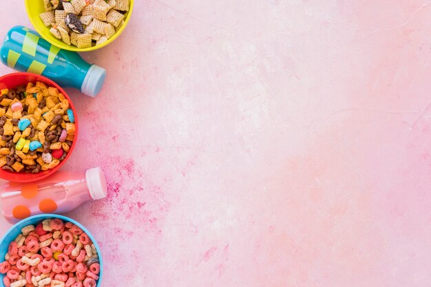 Tazones de cereales con botellas de leche en mesa rosa