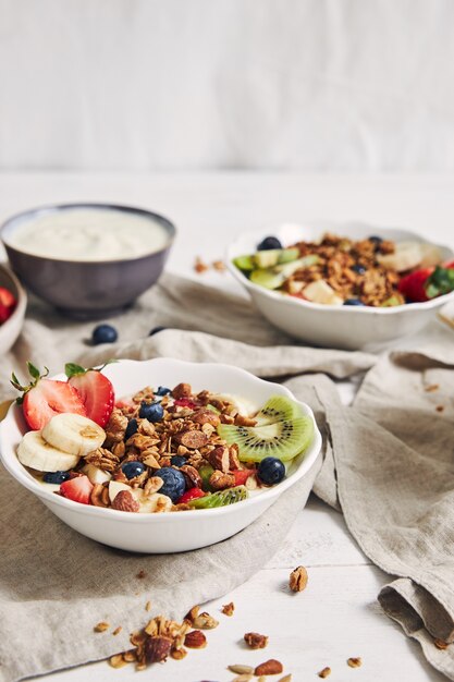 Tazones de granola con yogur, frutas y bayas sobre una superficie blanca