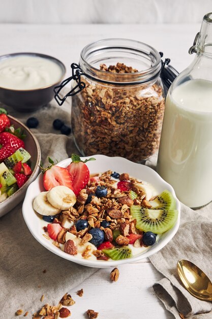 Tazones de granola con yogur, frutas y bayas sobre una superficie blanca