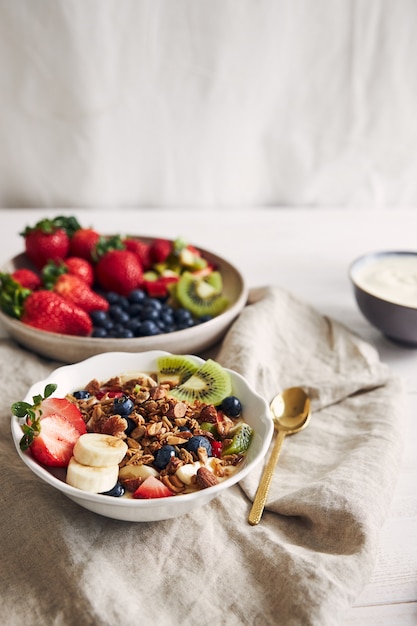 Tazones de granola con yogur, frutas y bayas sobre una superficie blanca