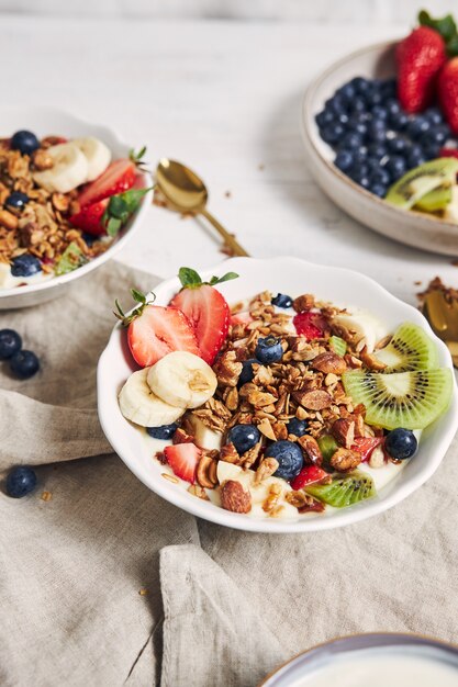 Tazones de granola con yogur, frutas y bayas sobre una superficie blanca