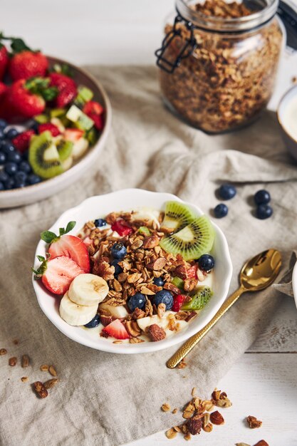 Tazones de granola con yogur, frutas y bayas sobre una superficie blanca