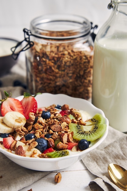 Tazones de granola con yogur, frutas y bayas sobre una superficie blanca