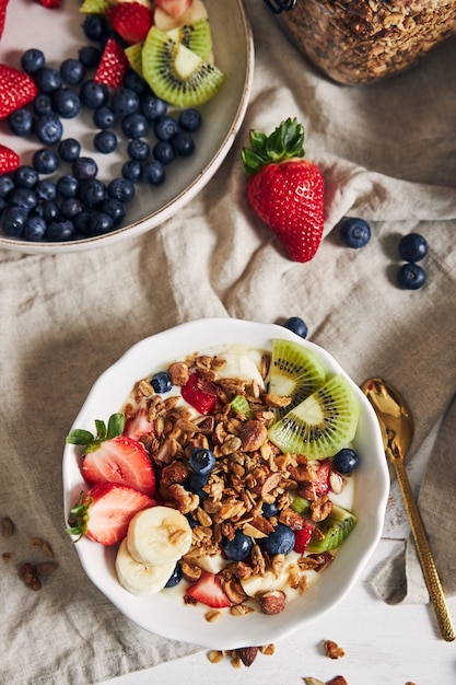 Tazones de granola con yogur, frutas y bayas sobre una superficie blanca