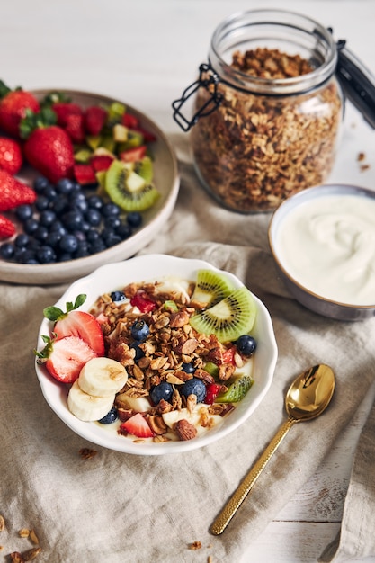 Tazones de granola con yogur, frutas y bayas sobre una superficie blanca