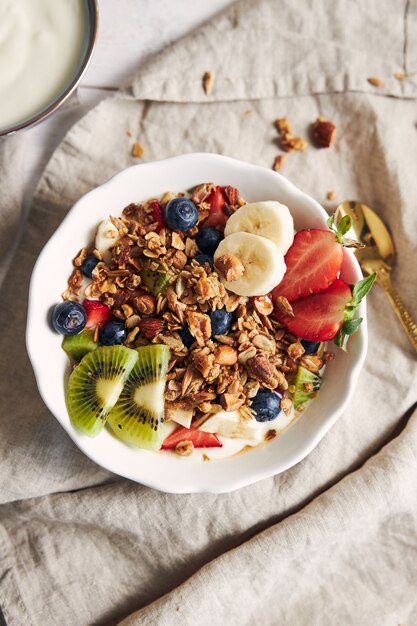 Tazones de granola con yogur, frutas y bayas sobre una superficie blanca