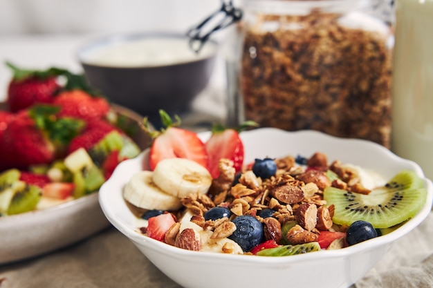 Tazones de granola con yogur, frutas y bayas sobre una superficie blanca