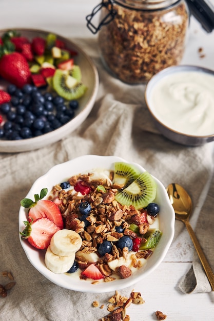 Tazones de granola con yogur, frutas y bayas sobre una superficie blanca