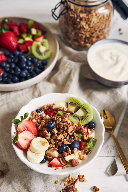 Tazones de granola con yogur, frutas y bayas sobre una superficie blanca