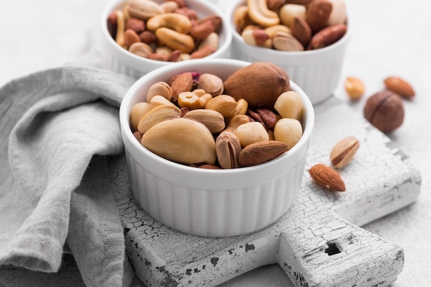 Tazones pequeños blancos llenos de variedad de nueces en la tabla de cortar