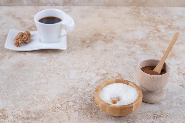 Tazones pequeños de café molido en polvo y azúcar junto a una taza de café y maní glaseado