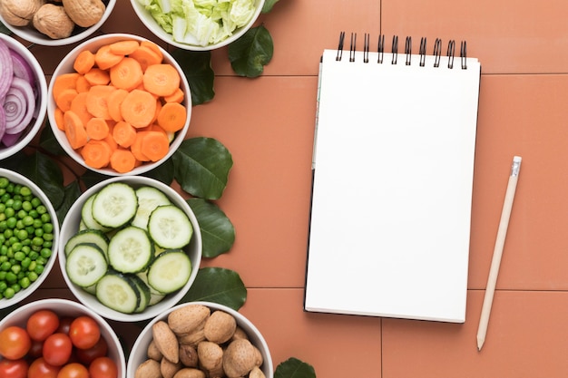 Foto gratuita tazones de verduras en rodajas y bloc de notas