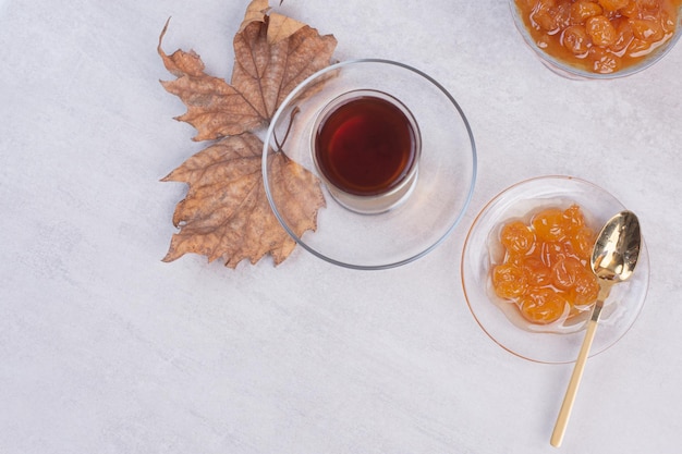 Té de aroma caliente con hojas y mermelada en la mesa blanca.