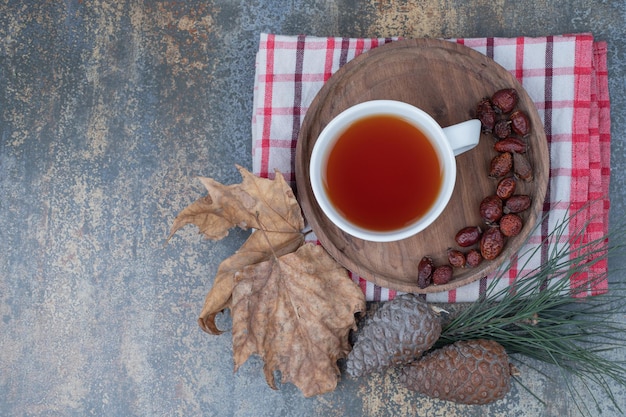 Té aromático en taza blanca con rosa mosqueta y piñas en mesa de mármol