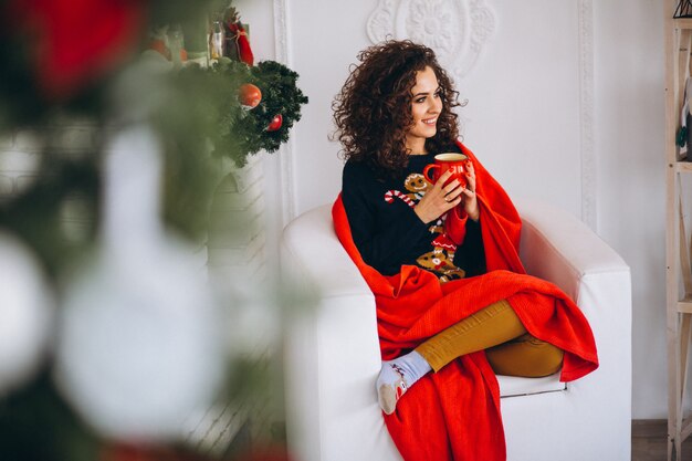 Té de consumición de la mujer joven por el árbol de navidad